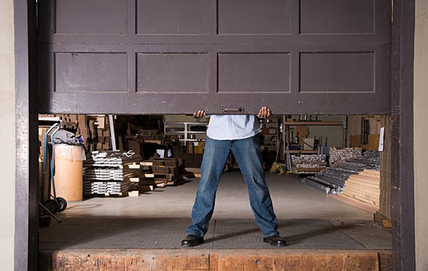 Man lifting up brown garage door that leads to construction supplies