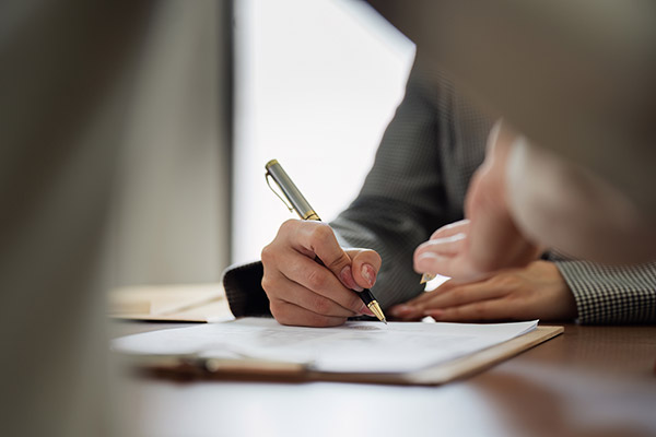 Businessperson signing Arizona commercial surety bond paperwork at an office desk.