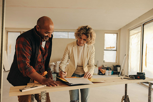 Contractor and client reviewing and signing construction plans on a makeshift table inside a partially renovated building.