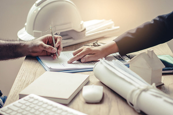 A person's hand points to the spot on a document for another person to sign.
