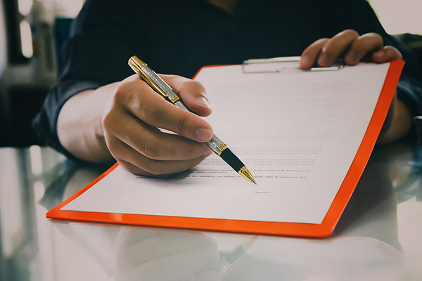 A person holding a pen with a document attached to a clipboard.