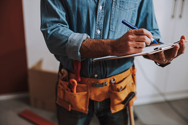 Close up of a contractor in a house writing on a clipboard.