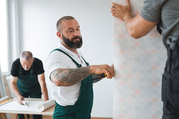 Three repair men working on repairing wallpaper in a living room.