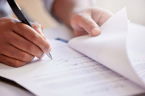 Close-up of hands holding papers up so that they can sign a paper on the bottom of a pile.