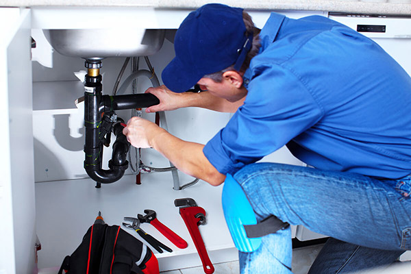 A plumber tightens pipes under a sink.