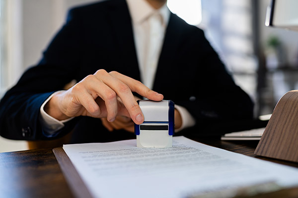 Man in a suit stamping a permit on a wooden desk.
